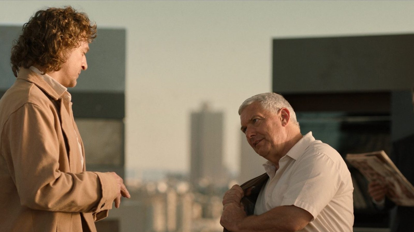 Dos hombres conversando en una azotea con la ciudad al fondo
